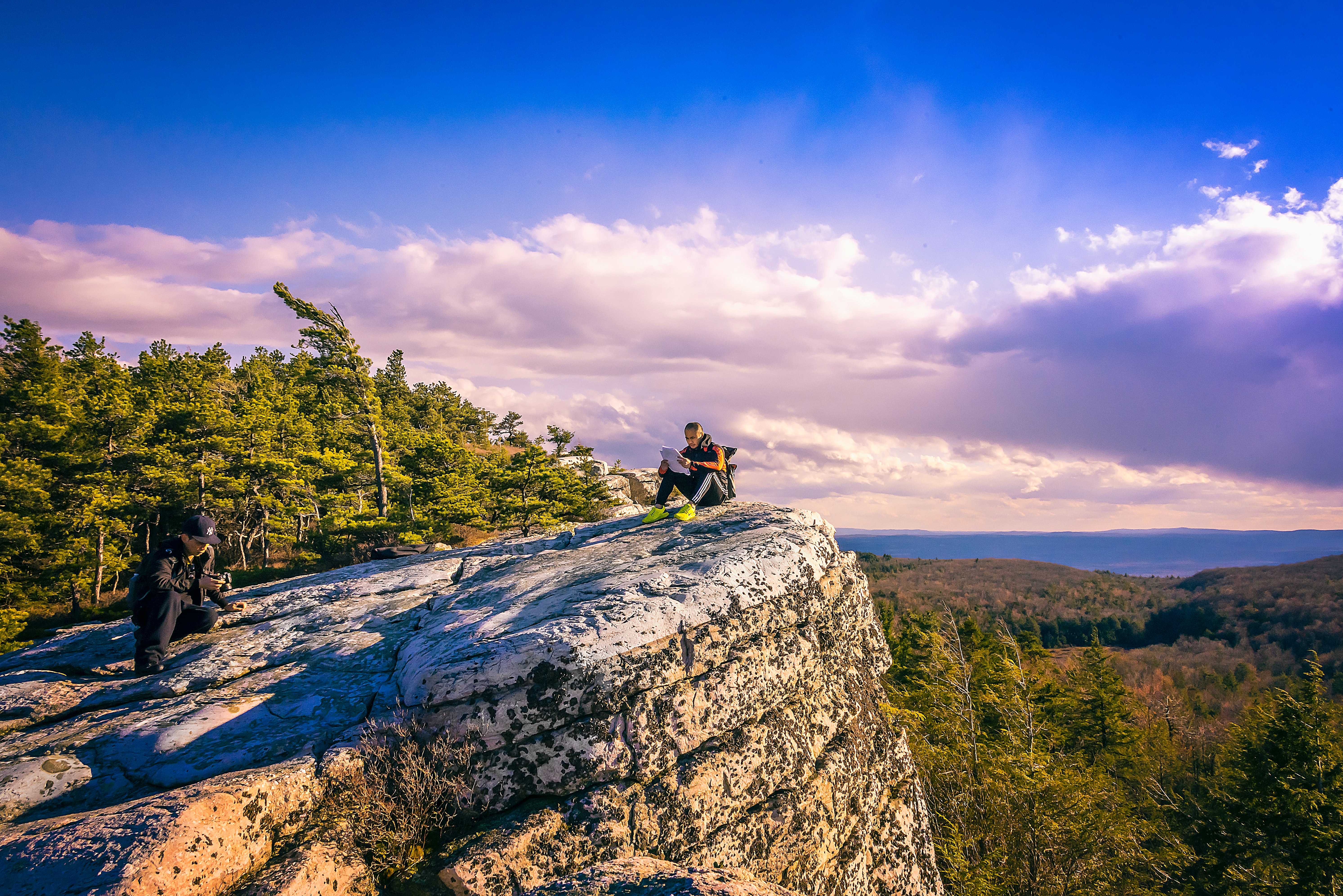 Man sitting atop a mountain staring into a beautiful sky with clouds.